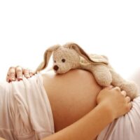 a pregnant woman with rabbit stuffie on belly- baby stuff