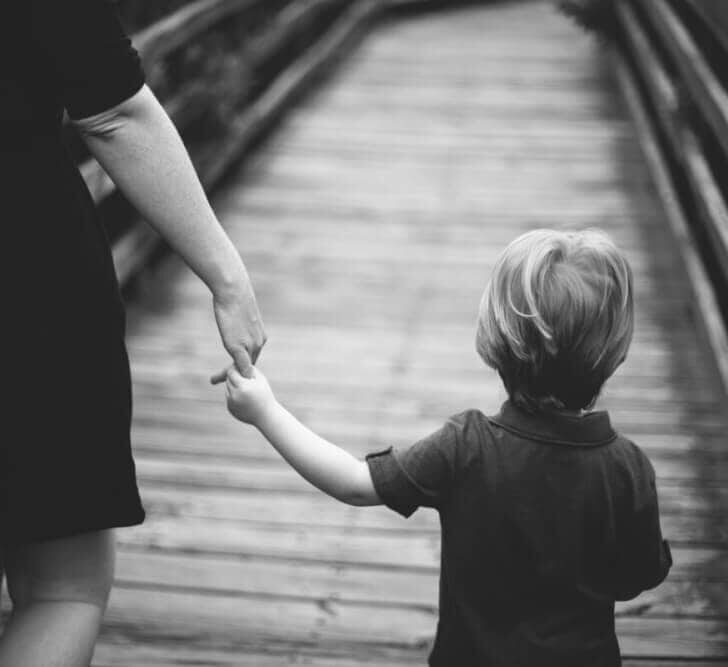 child holding the hand of an adult walking on a bridge