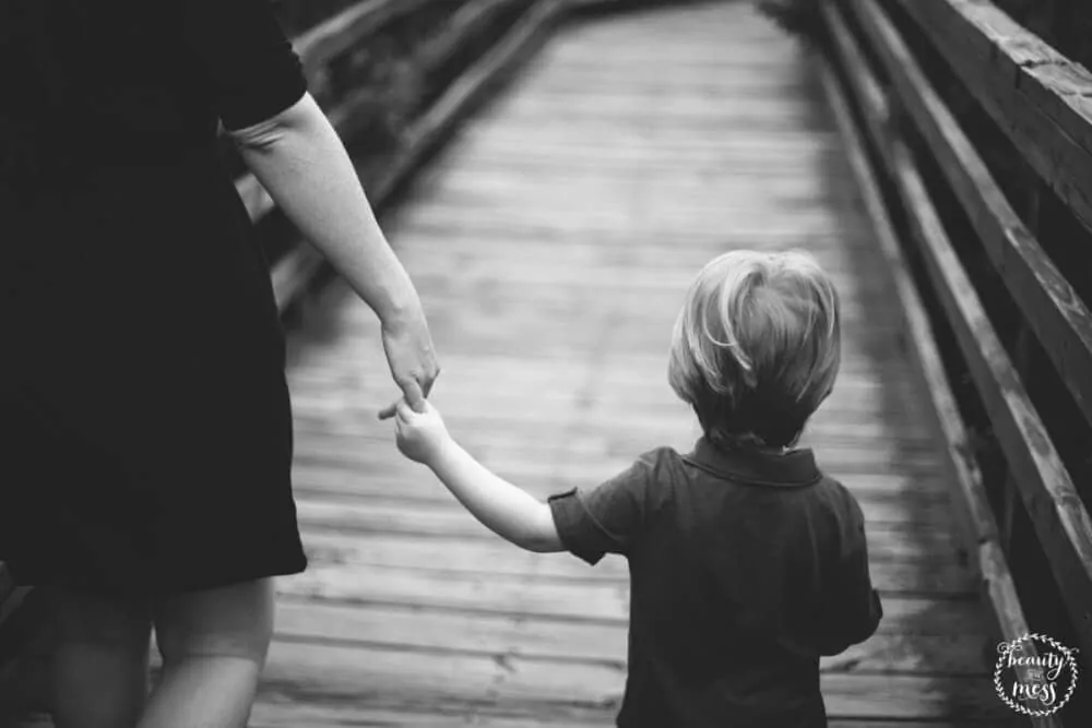 child holding the hand of an adult walking on a bridge