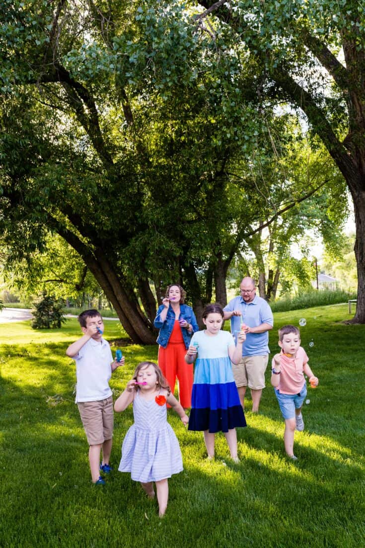 About Me | Family of six | Mom, Dad, four kids blowing bubbles in grass by a tree