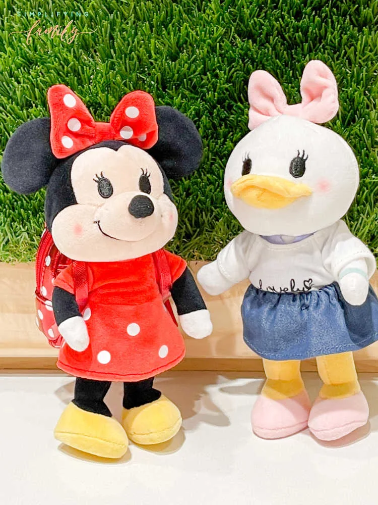 Disney's Minnie Mouse, and Daisy Duck Disney nuiMOs with Loungefly backpack in front of green grass wall with wood frame