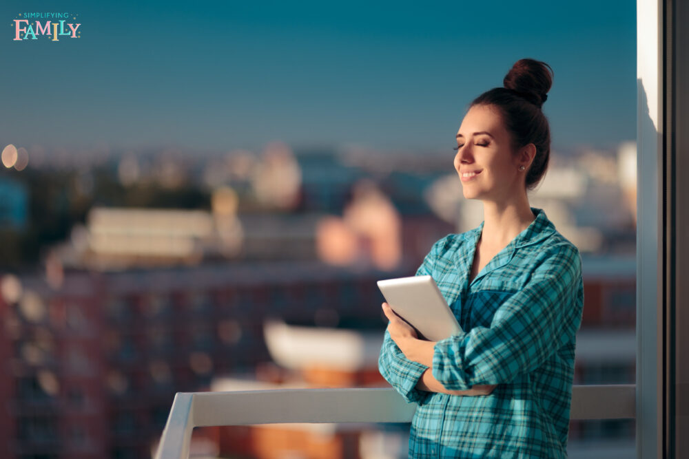 Woman standing on balcony with eyes closed in the morning holding her morning routine checklist