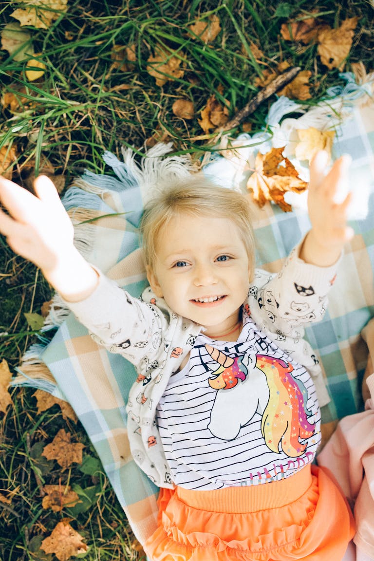 magical fall memories A cheerful young girl with blonde hair lays on a blanket outdoors, embracing the autumn vibes.